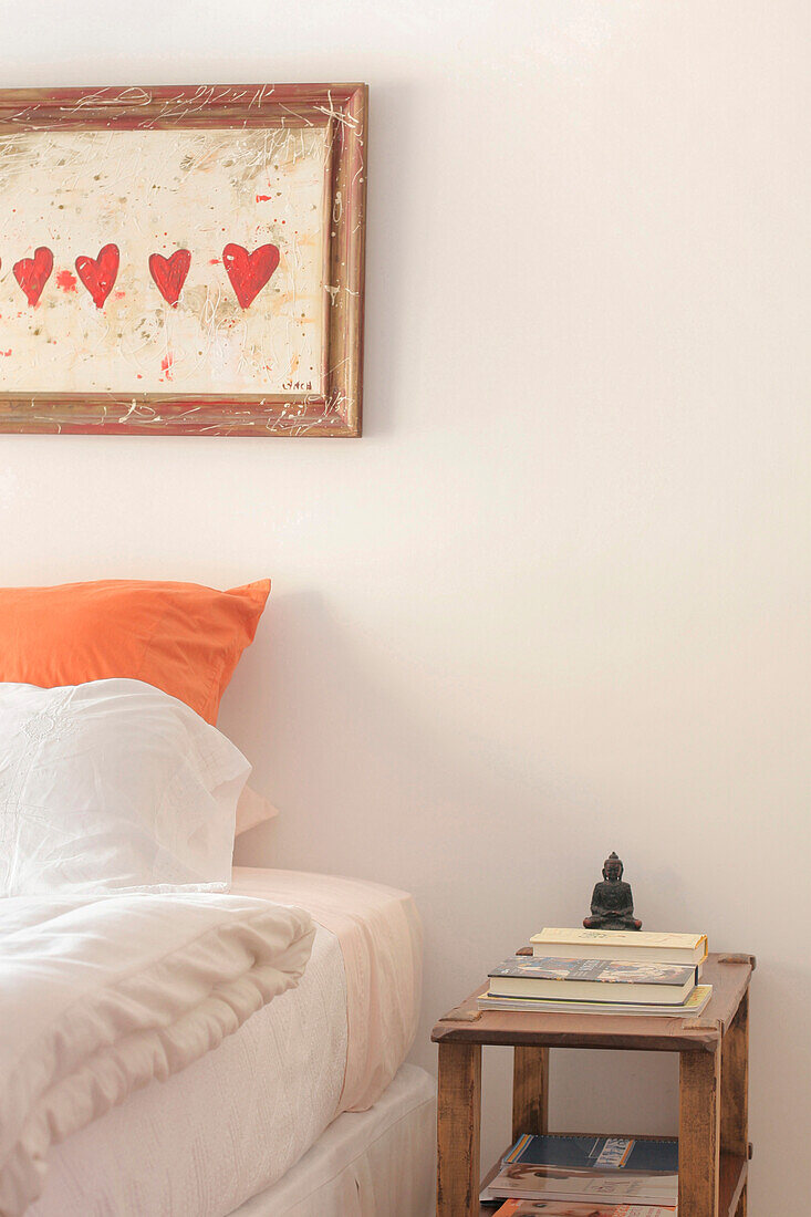 Schlafzimmer mit leuchtend orangefarbenem Kissen unter einem herzförmigen Kunstwerk
