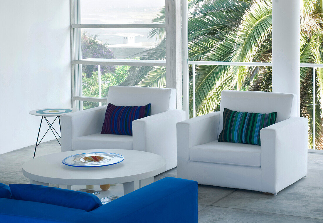 White living room with large windows and cushioned armchairs