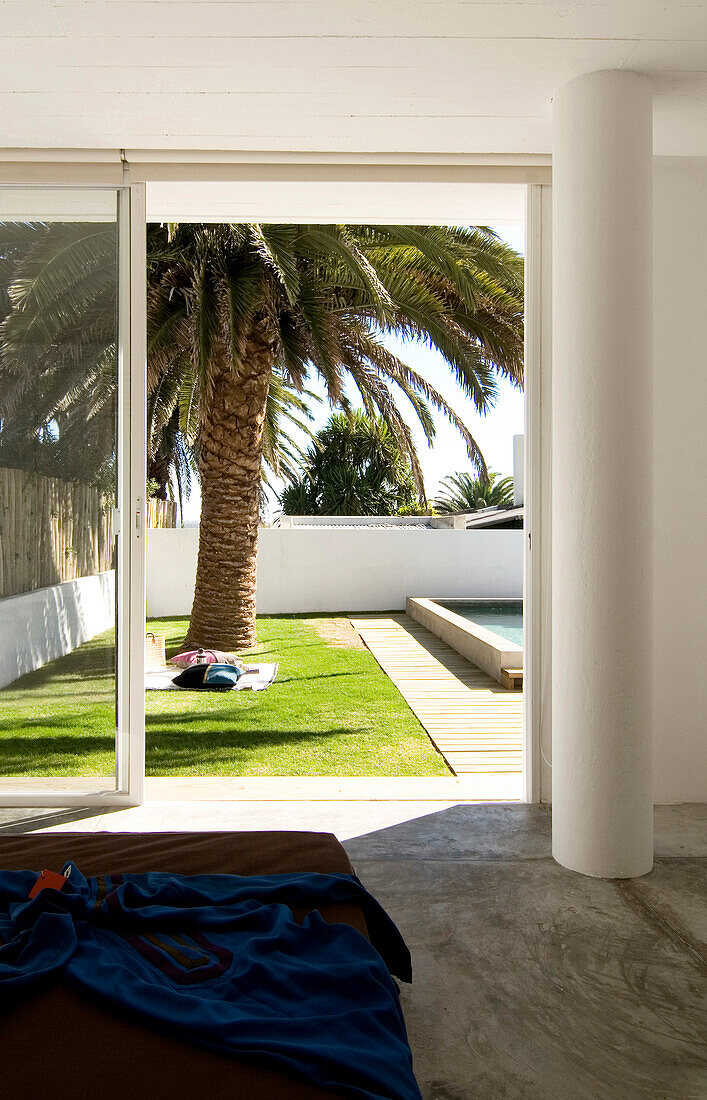 Bedroom door opens onto garden with palm tree and swimming pool