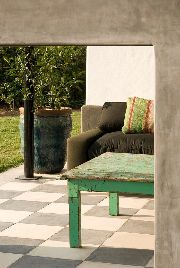Verwitterter Holztisch auf gefliester Veranda mit Sofa und Topfpflanze