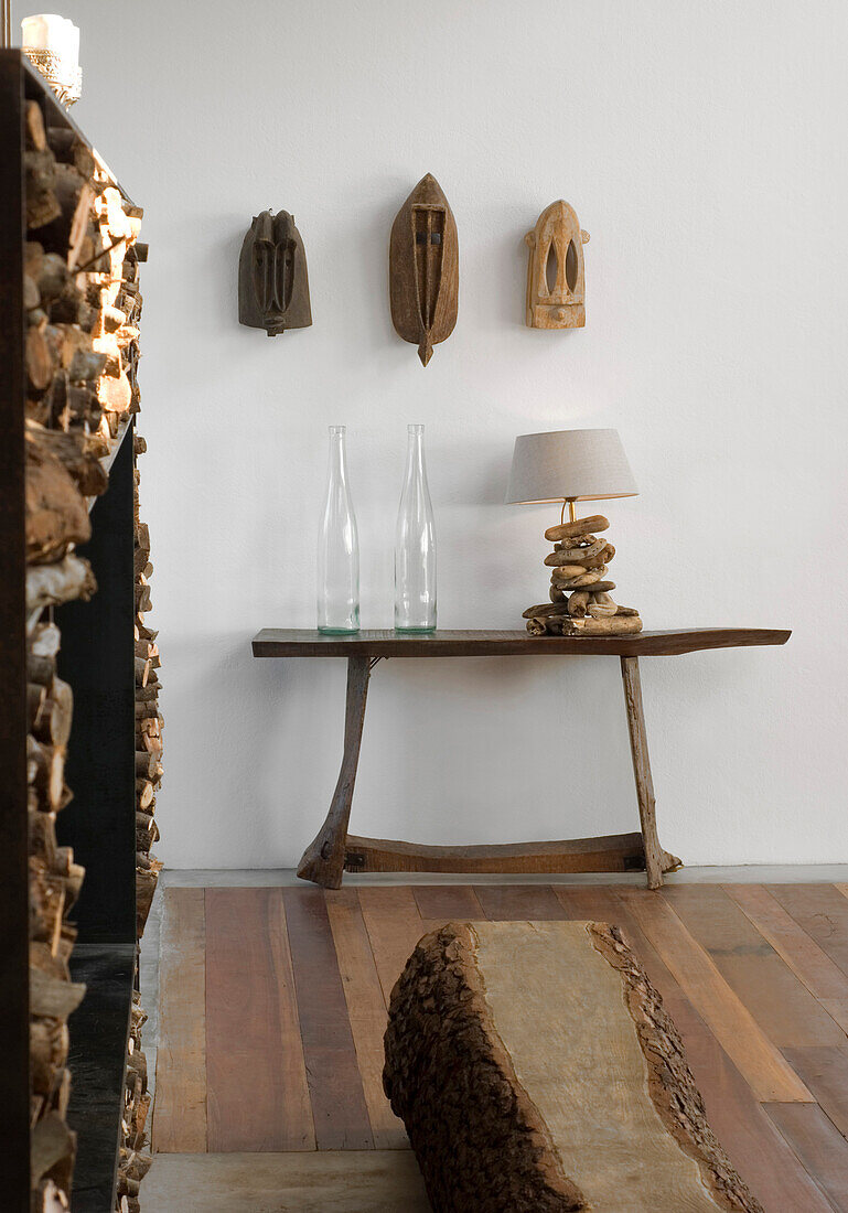 Three carved masks above wooden console table with lamp