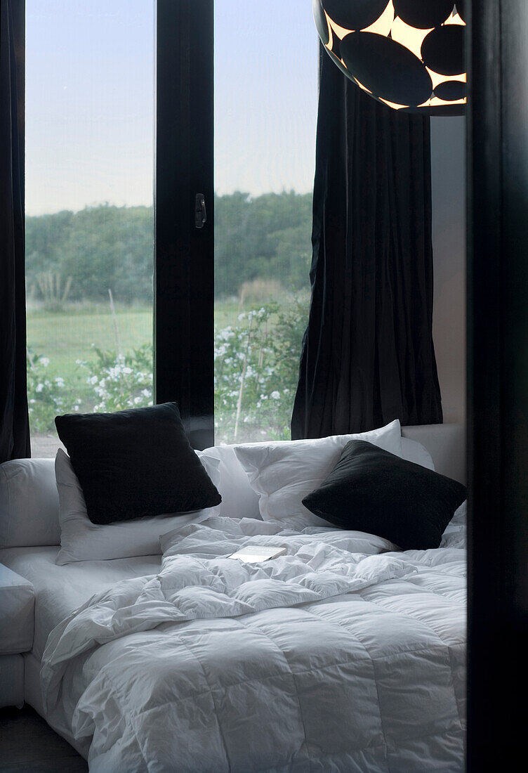 Ungemachtes kontrastreiches schwarz-weißes Bett am Fenster mit Blick aufs Land