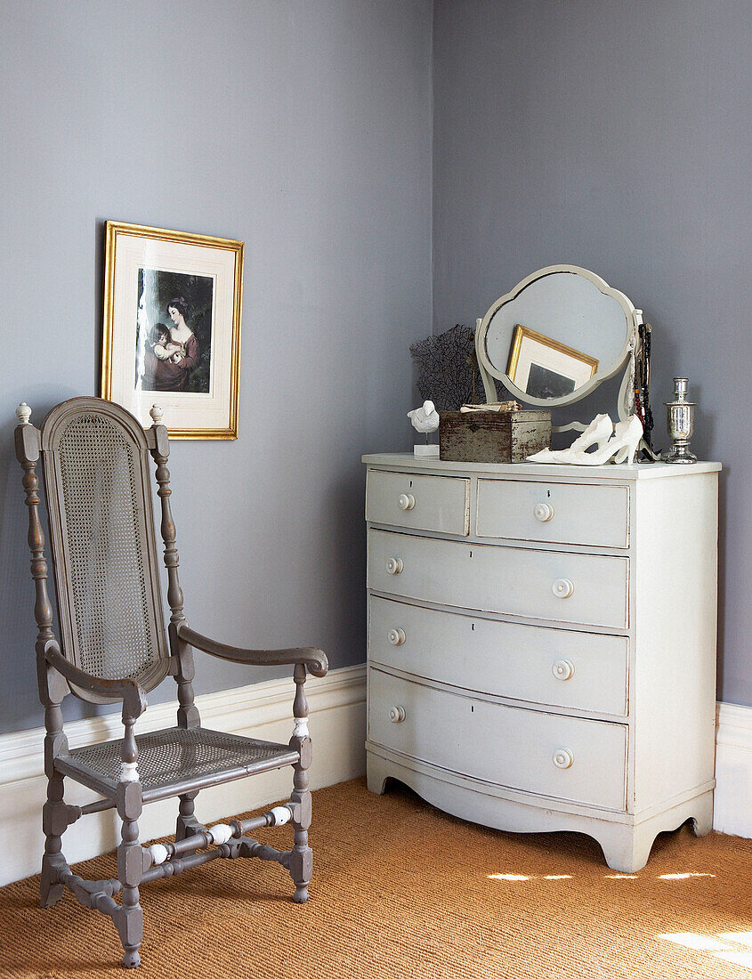 Bemalter Stuhl und Kommode in einer Ecke eines Schlafzimmers mit grauen Wänden und Kokosfasermatten