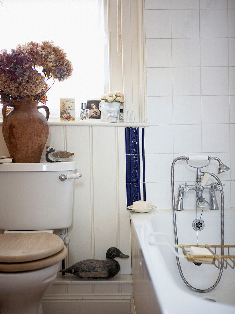 Keramikvase mit Trockenblumen auf Spülkasten in weiß gefliestem Badezimmer