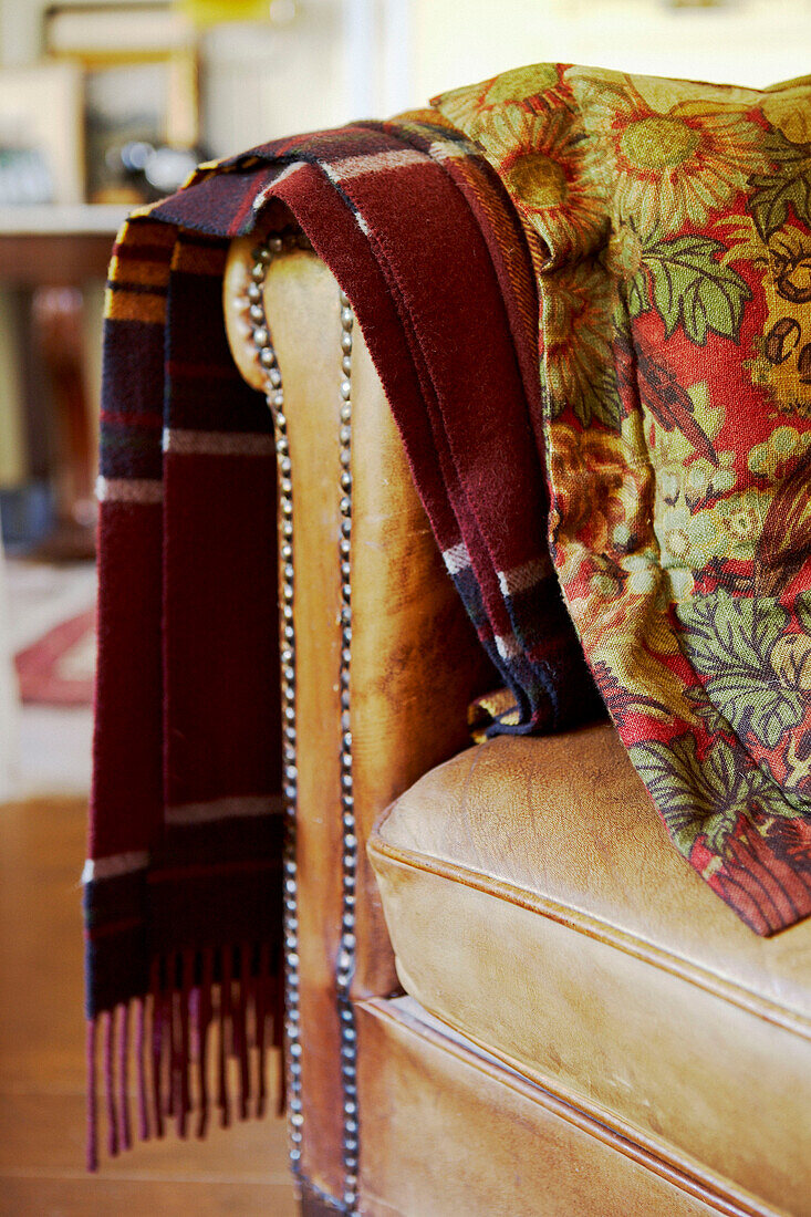 Woolen blanket and embroidered textile hang on the arm of a leather armchair