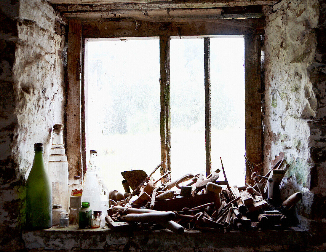 Alte Flaschen und landwirtschaftliche Geräte an einem sonnendurchfluteten Fenster