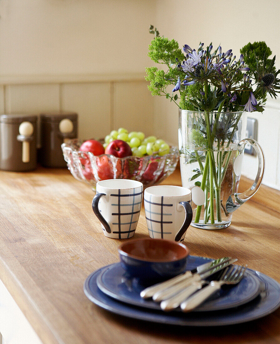 Geschirr und Tassen mit einem Krug mit Wildblumen auf einem hölzernen Esstisch