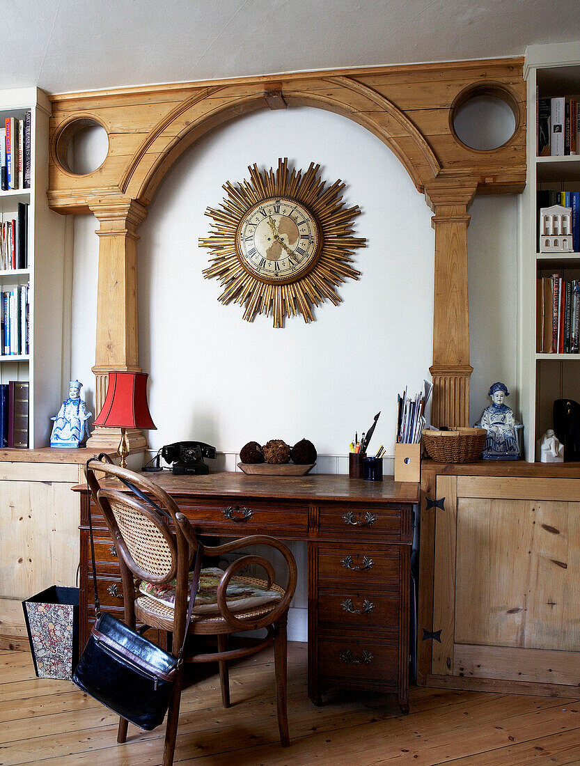Wicker backed chair at desk under carved architrave with solar clock