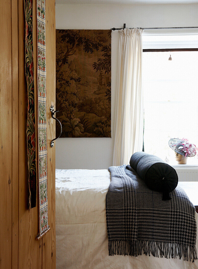 Wooden door opens to single bed with bolster and rug in sunlit bedroom 