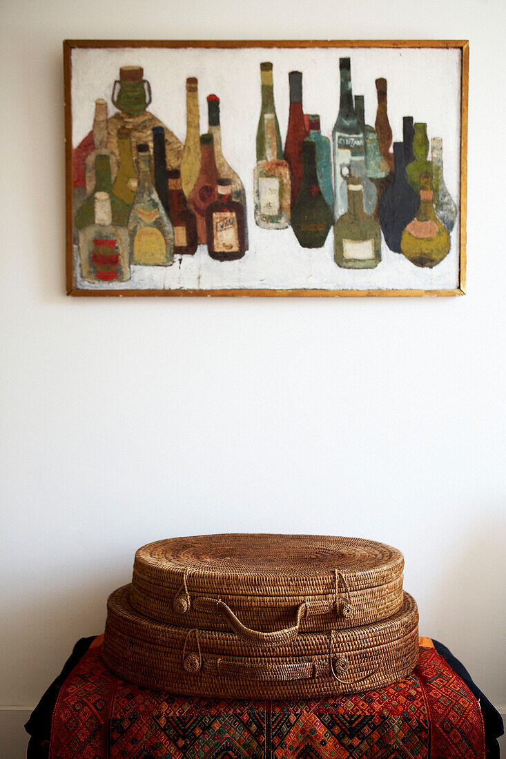 Two handmade baskets below artwork of variety of bottles 