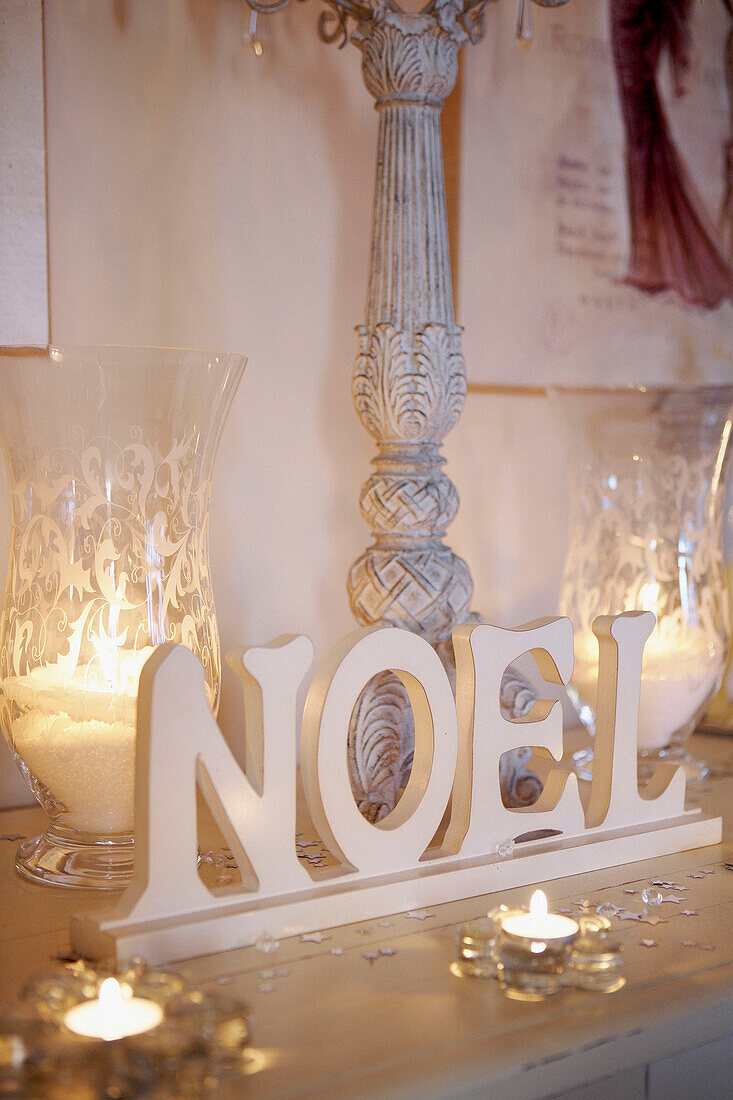 Lit candles with crystal glassware and lettering on painted tabletop