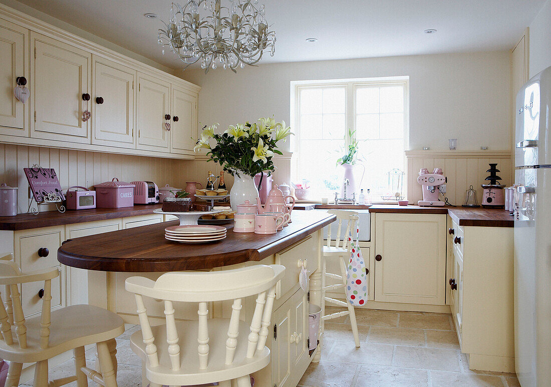 Sunlit kitchen with pink appliances and wooden island unit with painted white barstools
