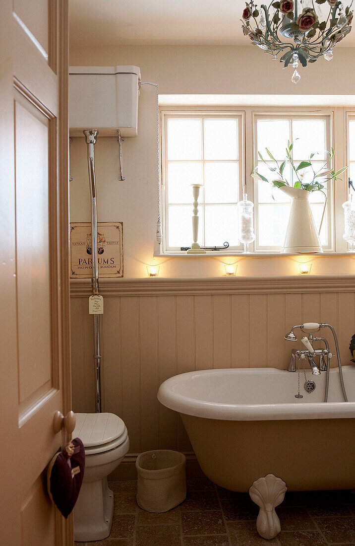 Rolltop-Badewanne unter sonnenbeschienenem Fenster in getäfeltem Badezimmer mit wandmontiertem Spülkasten