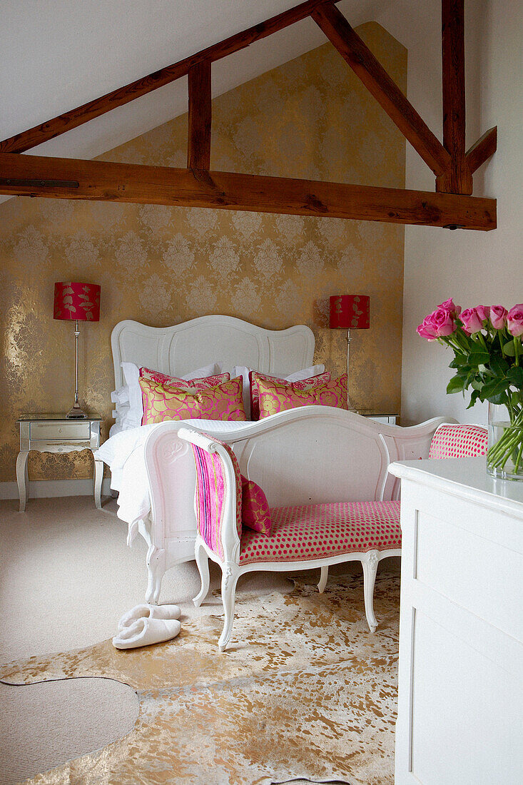 Elegantes Schlafzimmer mit freiliegendem Dachvorsprung im Kontrast zu bunten Stoffen, goldenen Tapeten und weißen Wänden und Möbeln