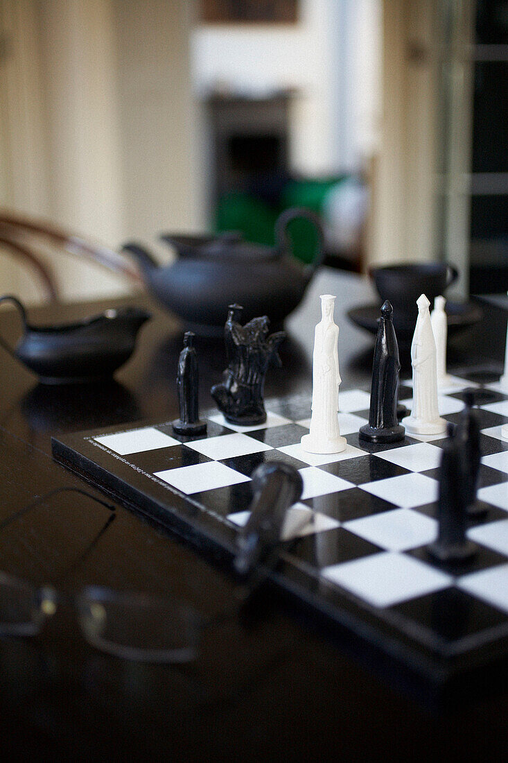 Schwarze und weiße Schachfiguren auf einem Tisch mit Teeservice