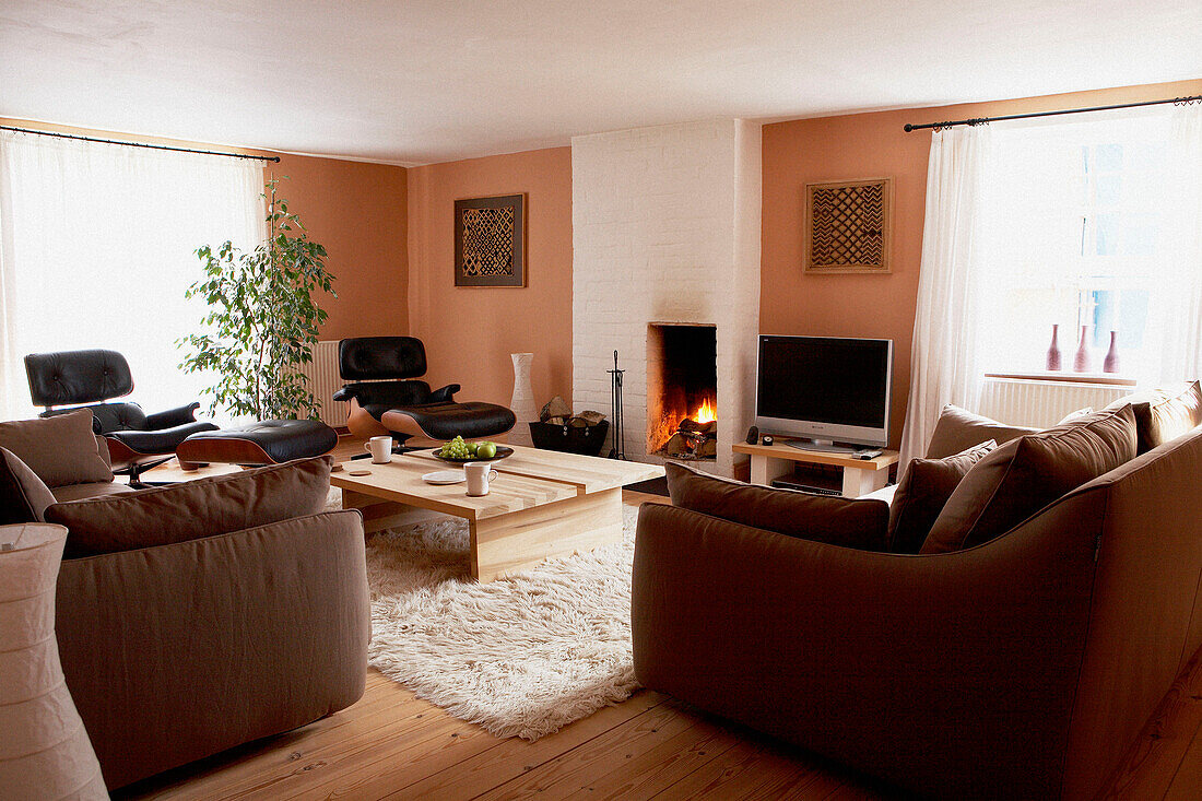 Braune Sofas mit Couchtisch und angezündetem Feuer in einem weiß gestrichenen Schornstein