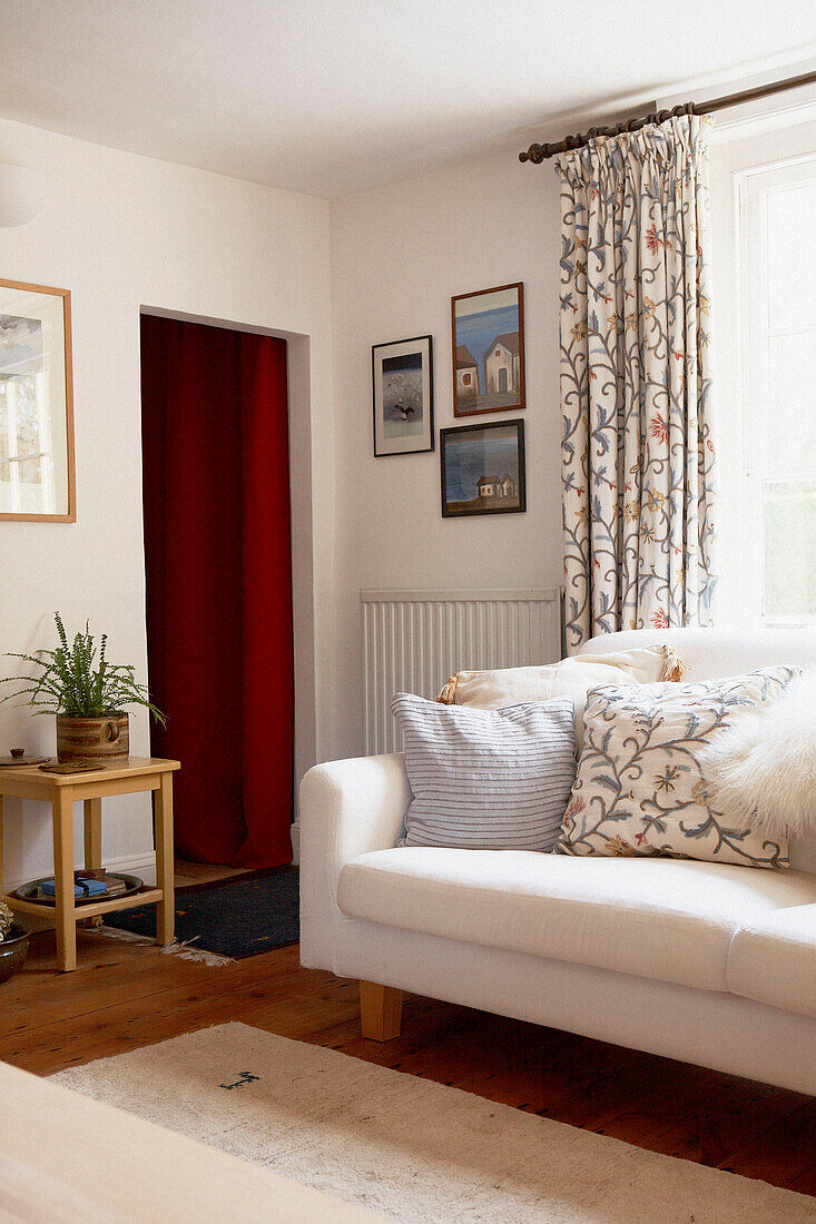 White sofa with co-ordinated cushion and curtains in living room with open doorway