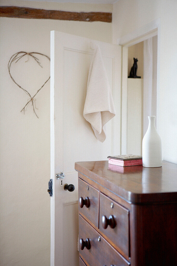 Weiße Vase auf Holzkommode im Schlafzimmer mit offener Tür