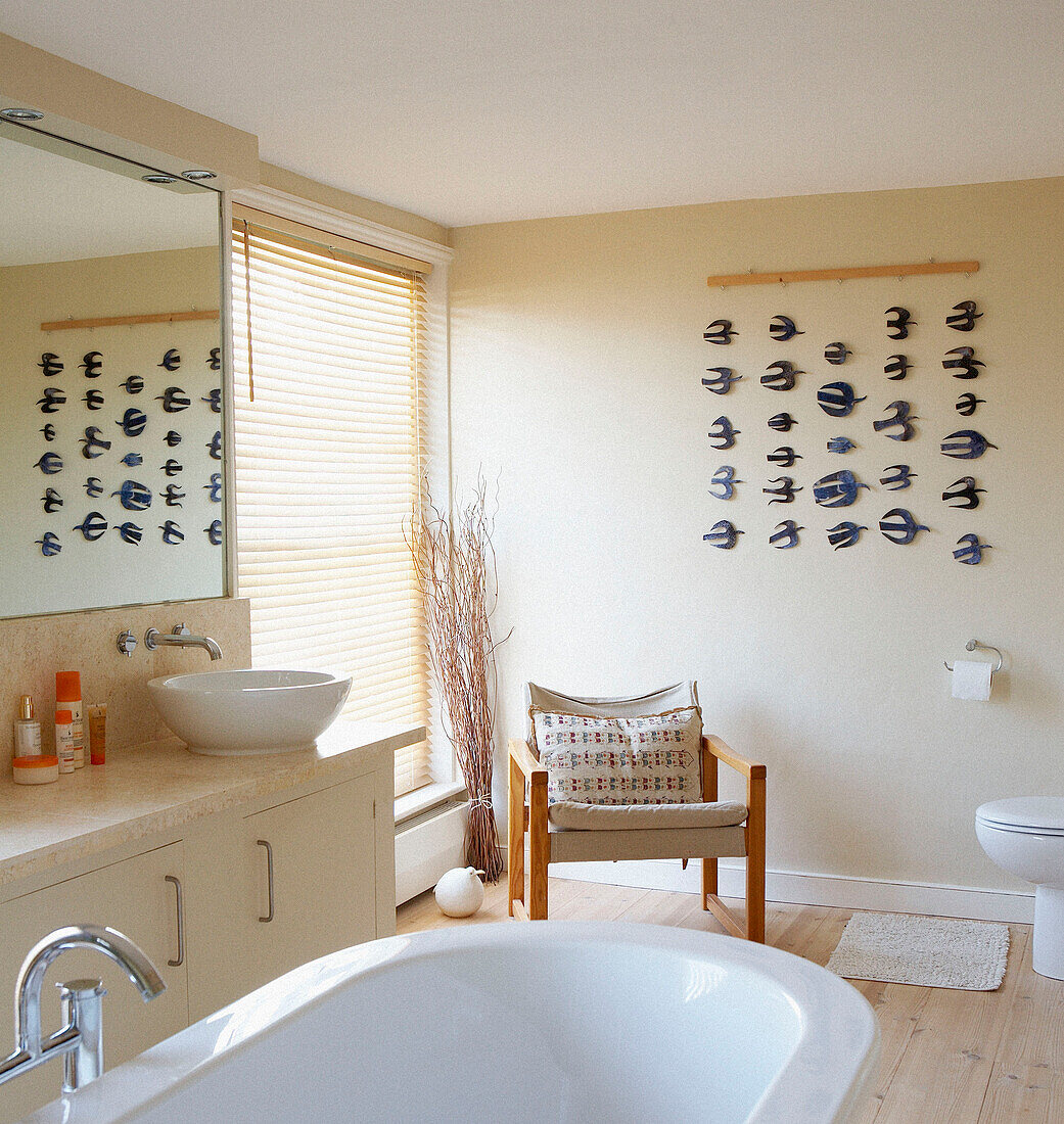 Freistehende Badewanne in einem sonnendurchfluteten Badezimmer mit einem Stuhl am Spiegel und einer Kunstinstallation