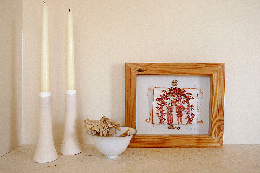 Cremefarbene Kerzen und eine Schale mit Trockenblumen mit gerahmtem Kunstwerk