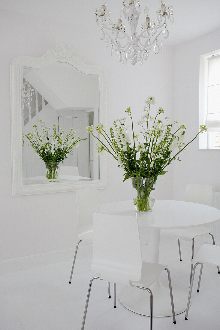 Vase of flowers on reflected in mirror of all white dining room