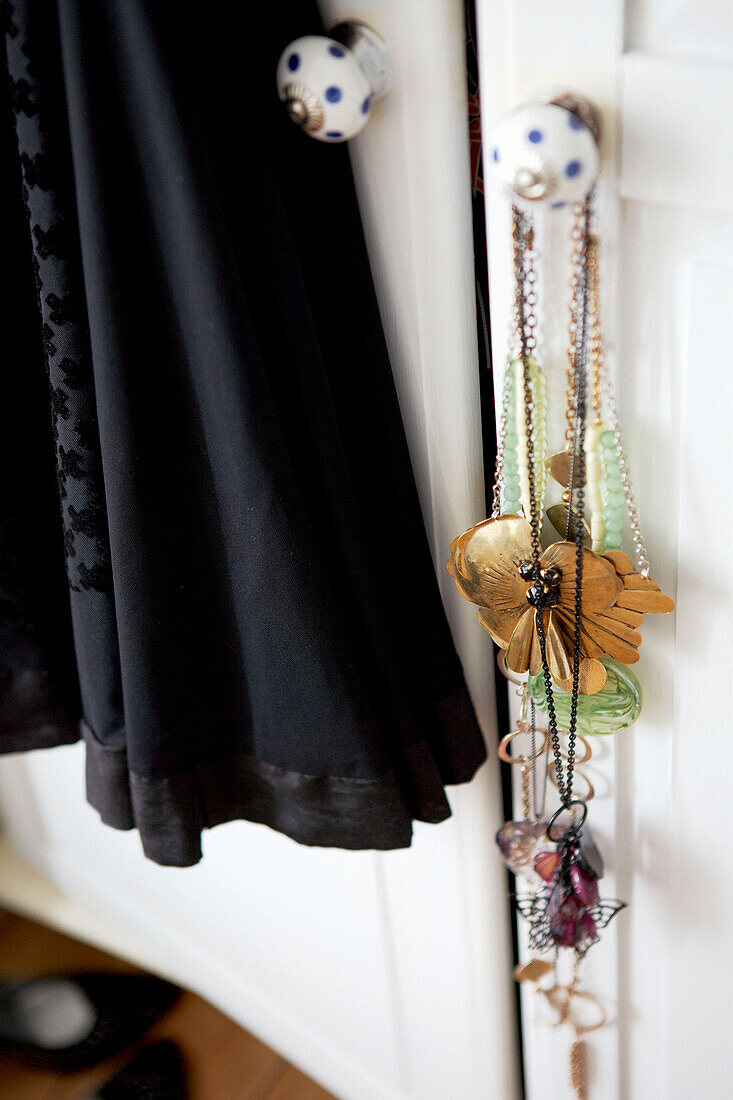 Halsketten und schwarzes Kleid hängen an bemalten Schranktüren