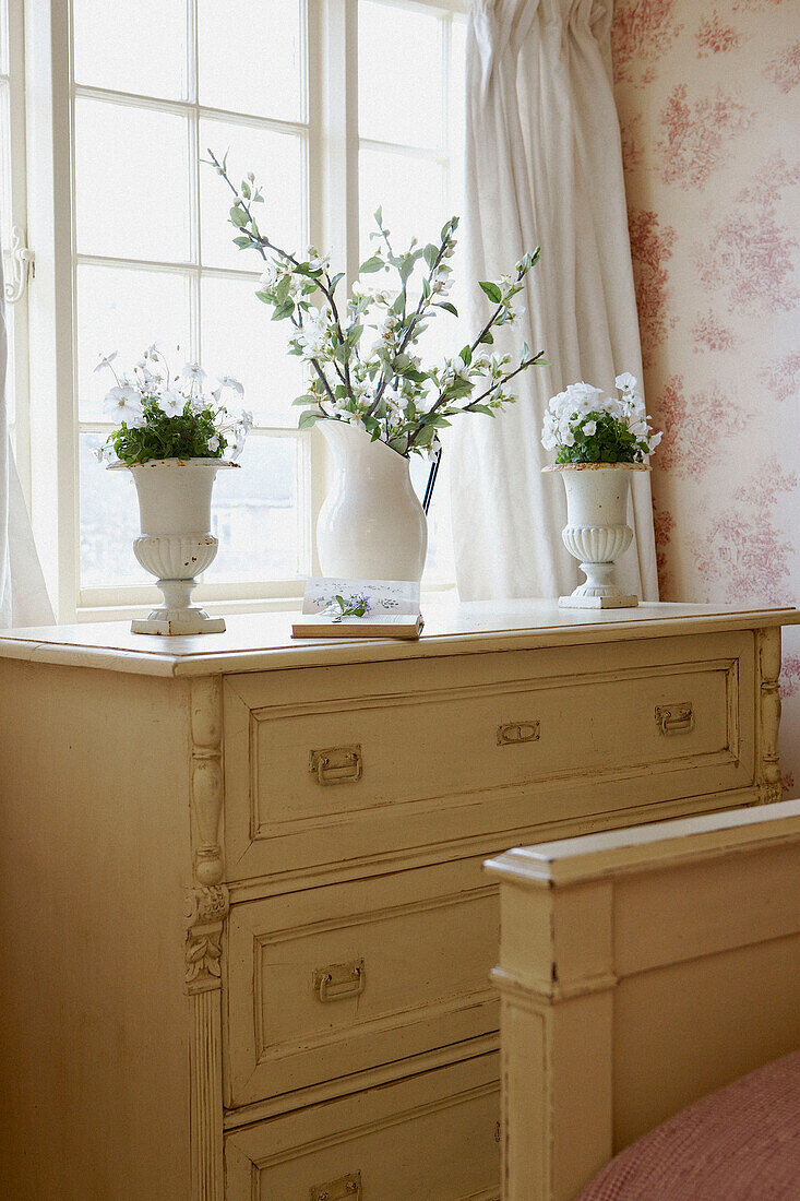 White flowers on painted chest of drawers in sunlit window