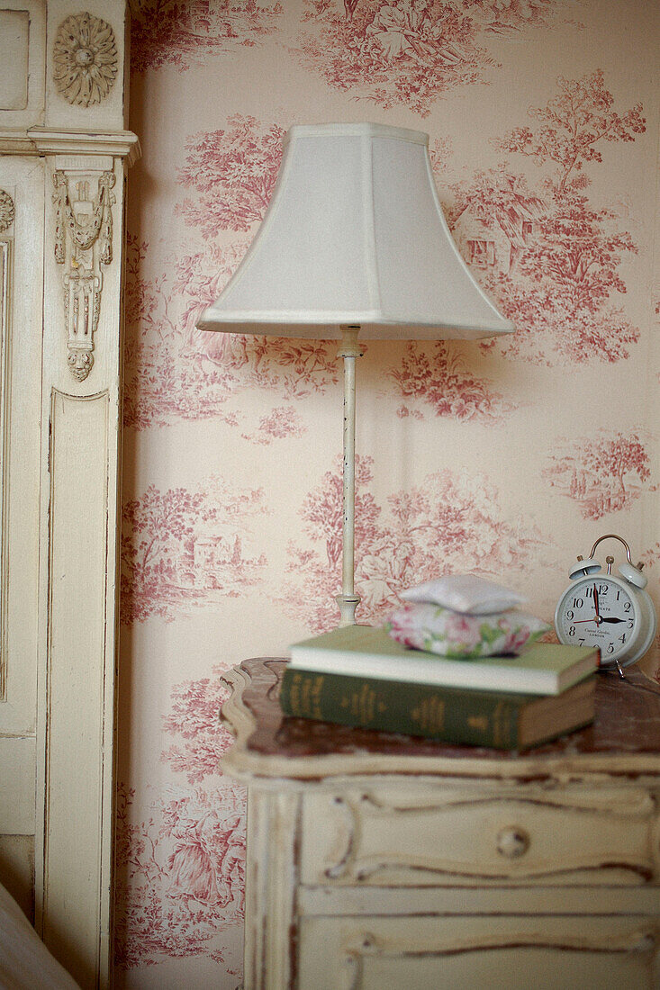 Lamp on bedside table with books and alarm clock