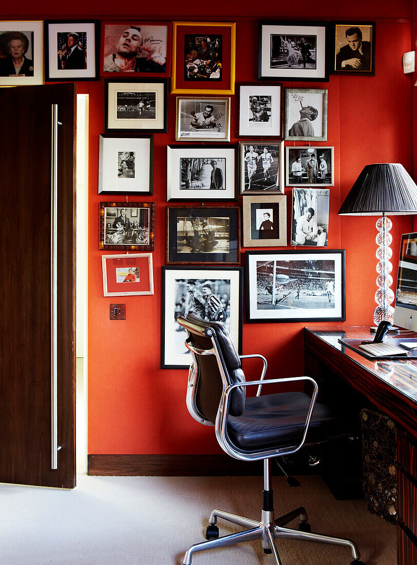 Schwarzer Leder-Bürostuhl in rot gestrichenem Arbeitszimmer mit Ausstellungsporträts