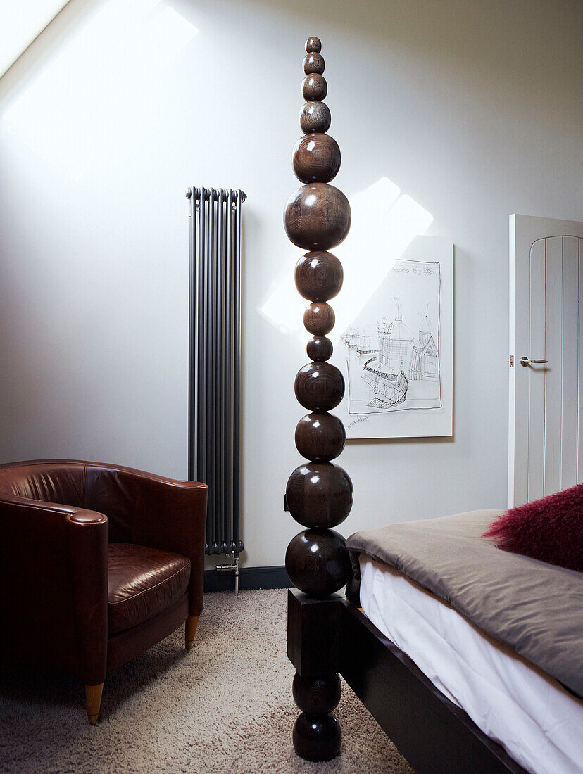 Sculptural bedpost and leather armchair with wall mounted radiator in Richmond school church conversion