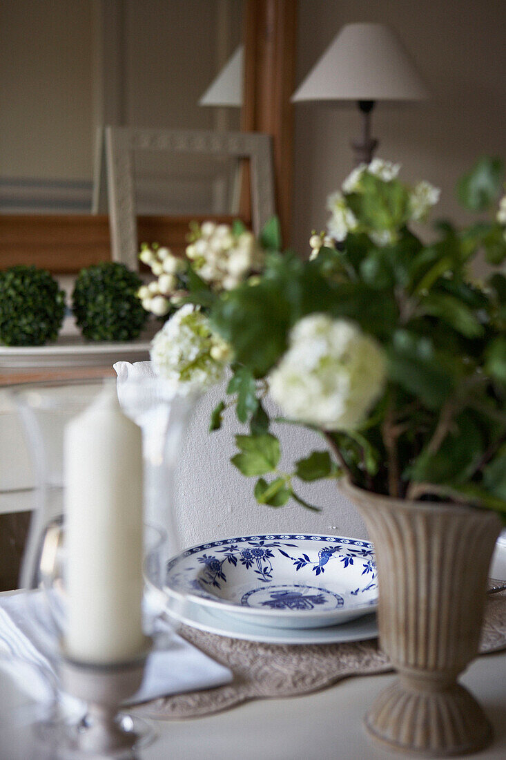Gemusterter Teller und Kerze mit Schnittblumen auf dem Esstisch