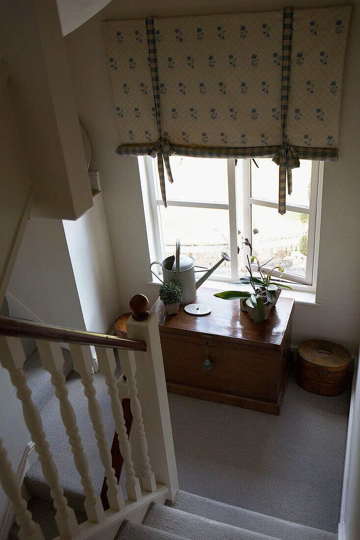 Window treatment above wooden travelling chest on staircase landing