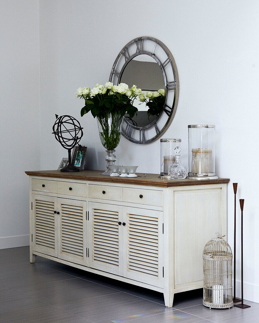 Painted sideboard with vase of white roses and metallic mirror with roman numerals