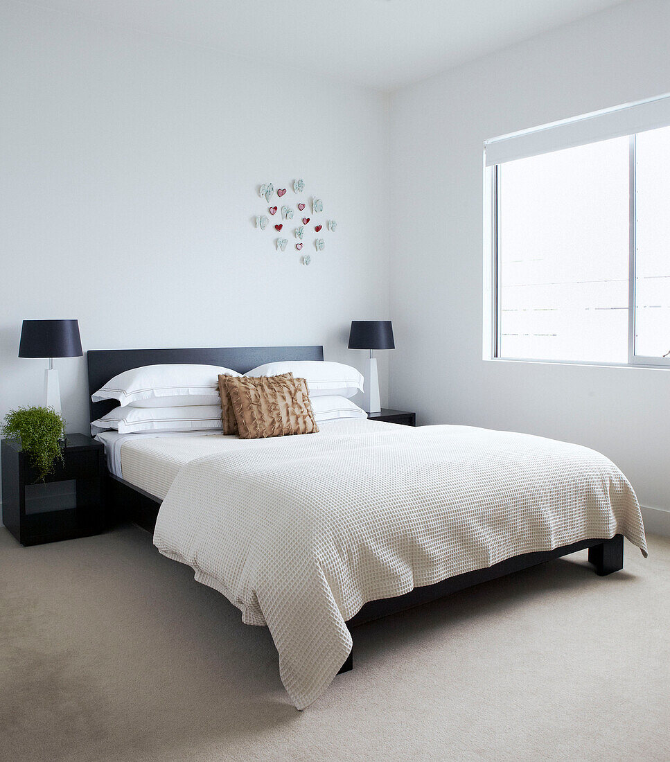 Doppelbett in sonnenbeschienenem Zimmer mit passenden Nachttischlampen und Wanddekoration aus Papier