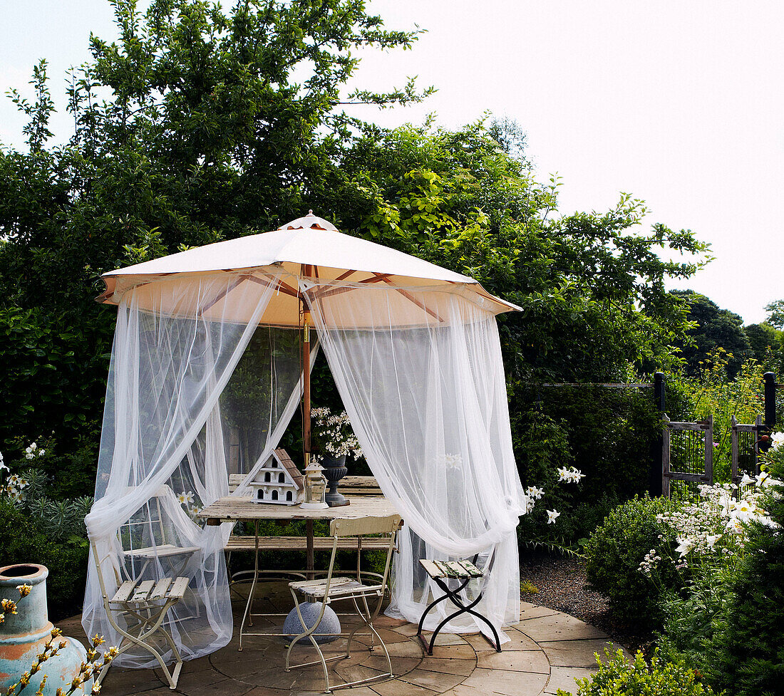 Sonnenschirm mit Moskitonetz auf Veranda mit Klappstühlen und Tisch