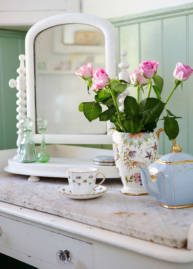 Bemalter Tisch mit Marmorplatte und Kippspiegel mit dekorativem Porzellan und Vase mit rosa Rosen