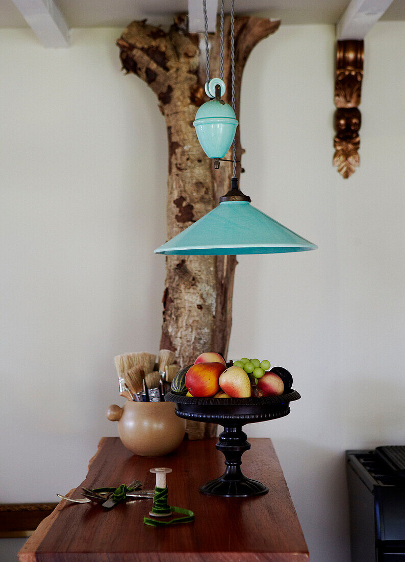 Türkisfarbene Pendelleuchte hängt über einem Tisch mit Baumstammhalterung