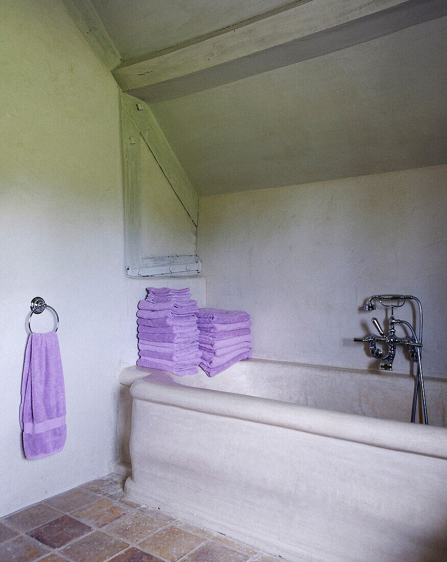 Gefaltete fliederfarbene Handtücher auf einer Badewannenverkleidung in einem Landhaus