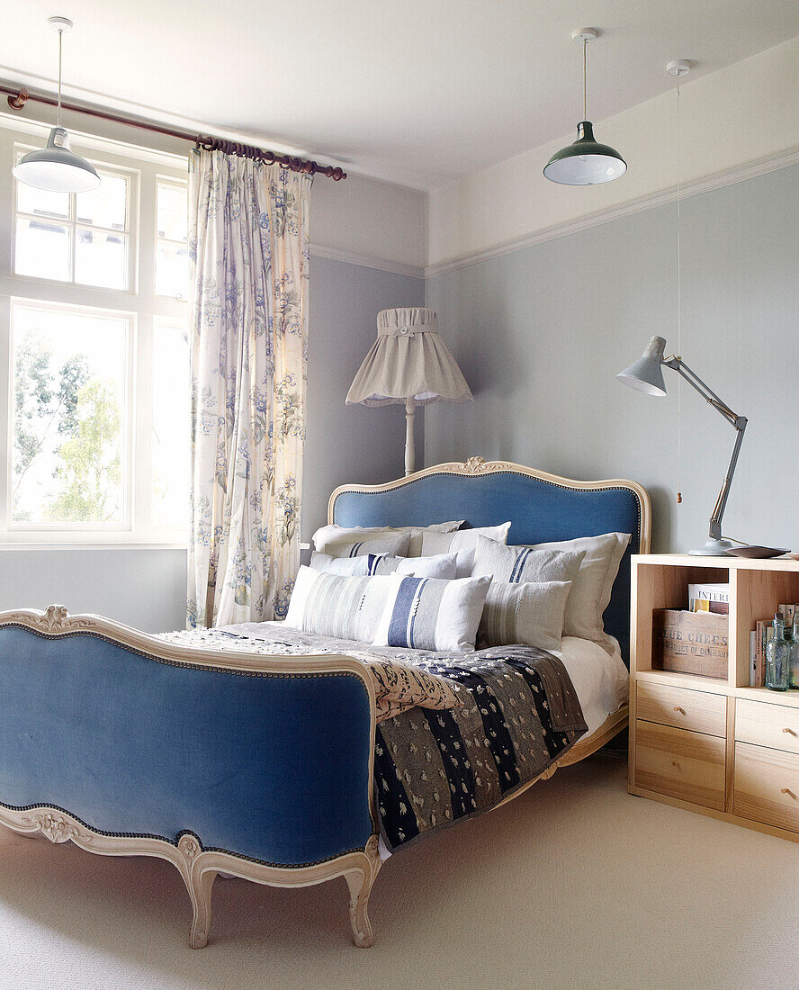 Blaue Kopf- und Fußteile auf einem Bett am Fenster mit hölzernem Nachttisch