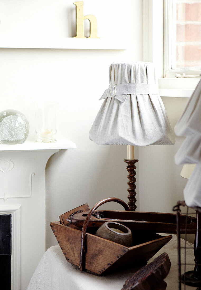 Fabric covered lampshade with wooden objects on side table below window in country house