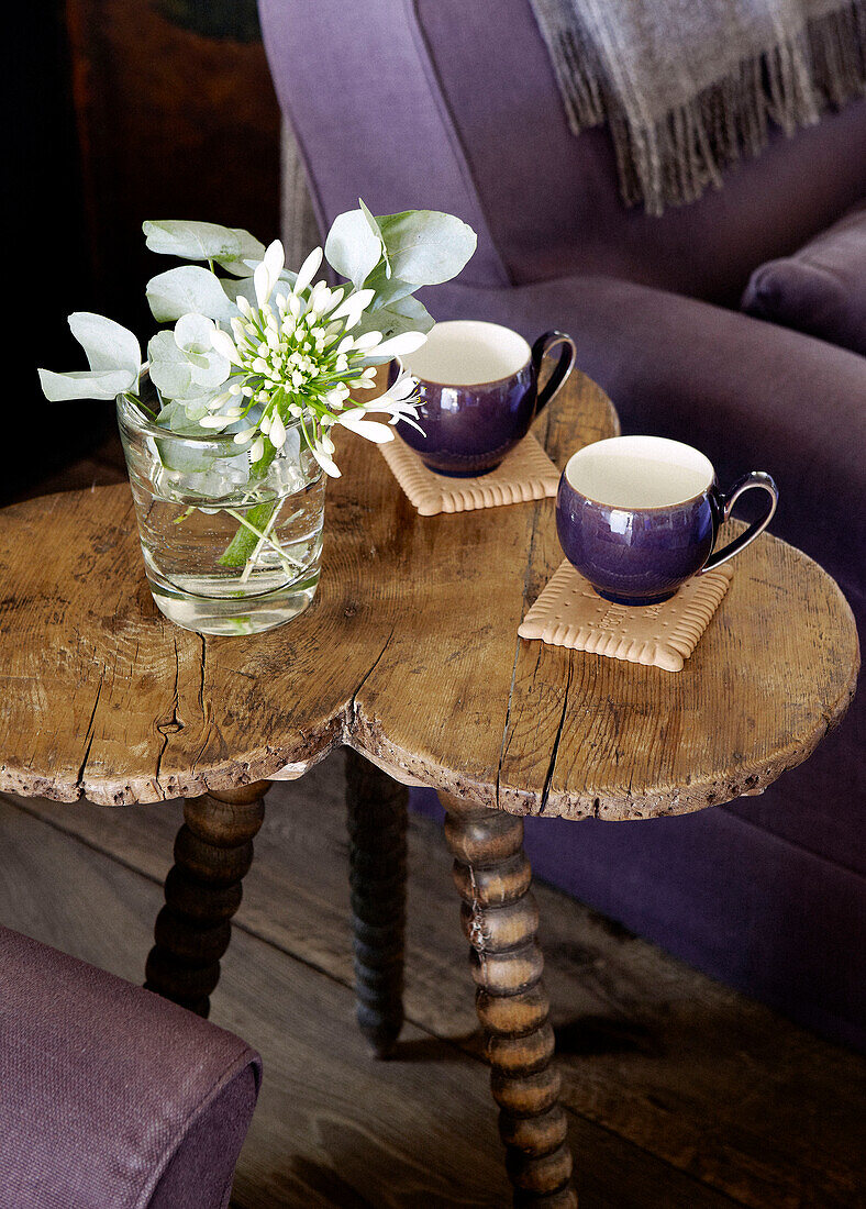 Two purple cups and cut flowers in glass on rough hewn side table in country home