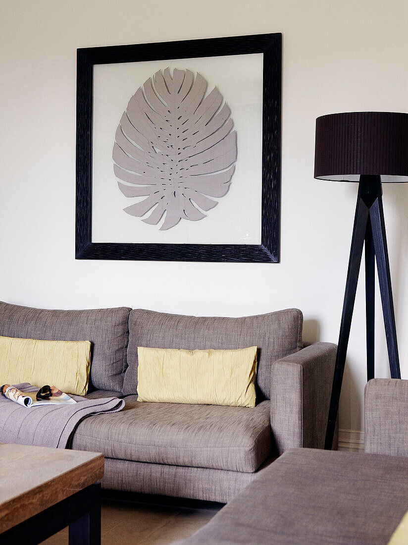Goldene Kissen auf grauem Sofa mit Stehlampe und Kunstwerk mit Blattmotiv im Rahmen