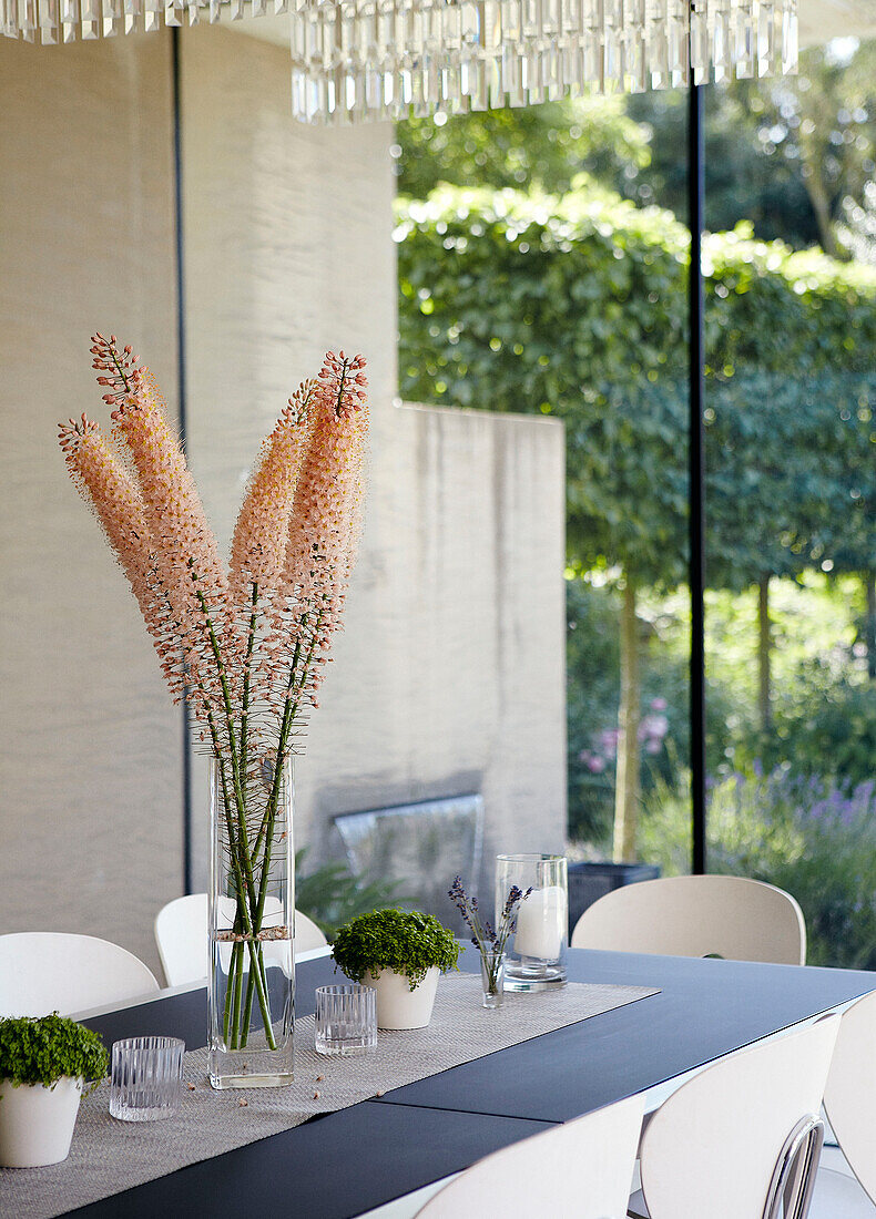 Cut flowers on dining table with view through glass wall to garden exterior