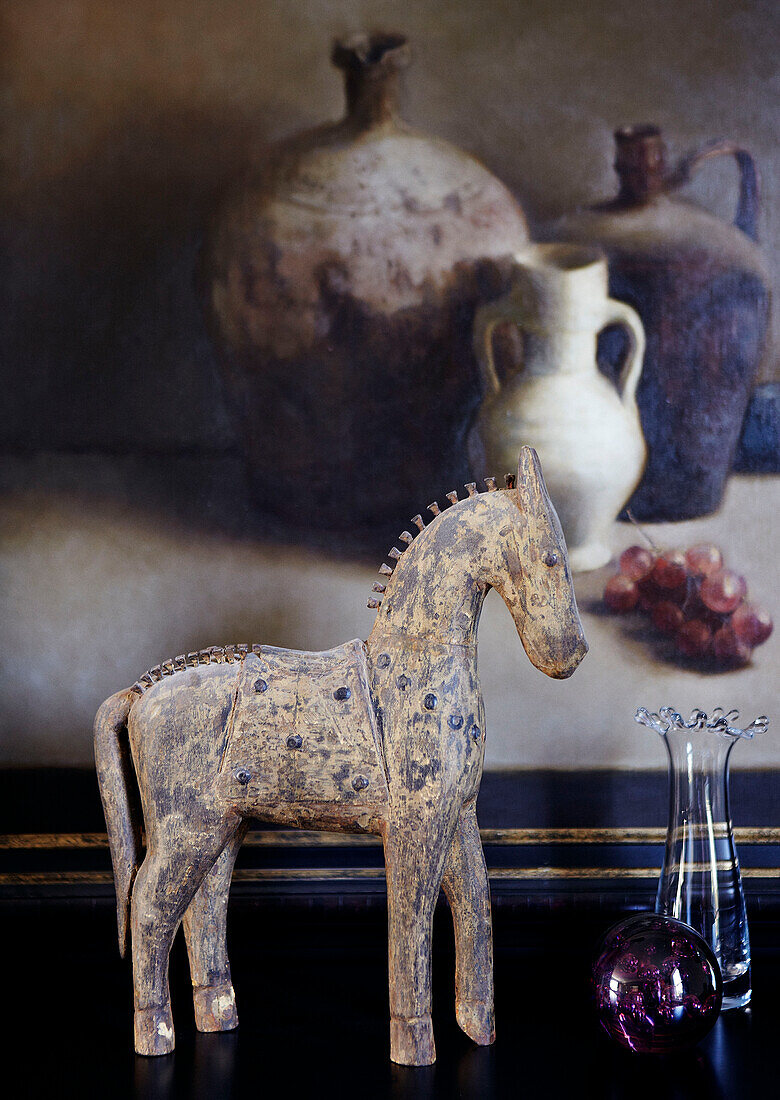 Model horse and glassware in front of artwork