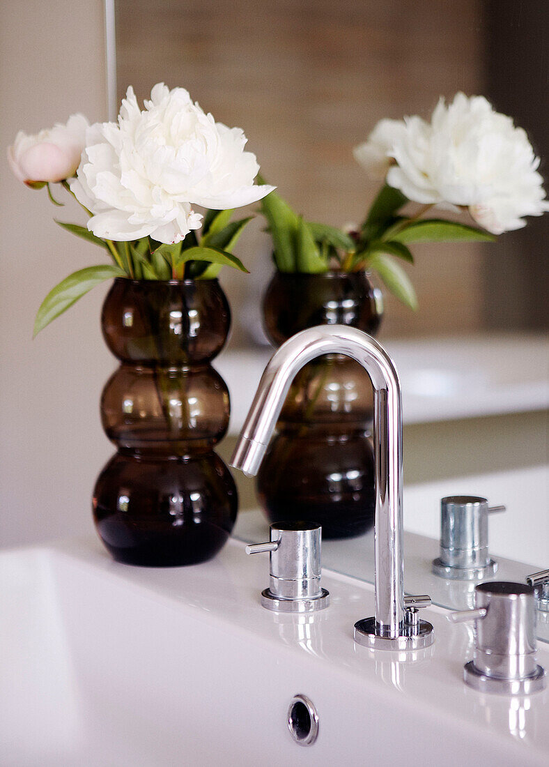 Cut peony reflected in mirror in vase on washbasin