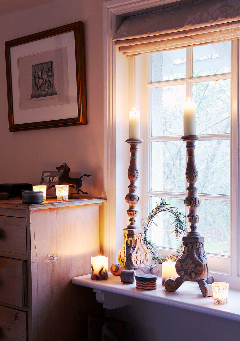 Lit candles in carved wooden candlestick on windowsill of country home