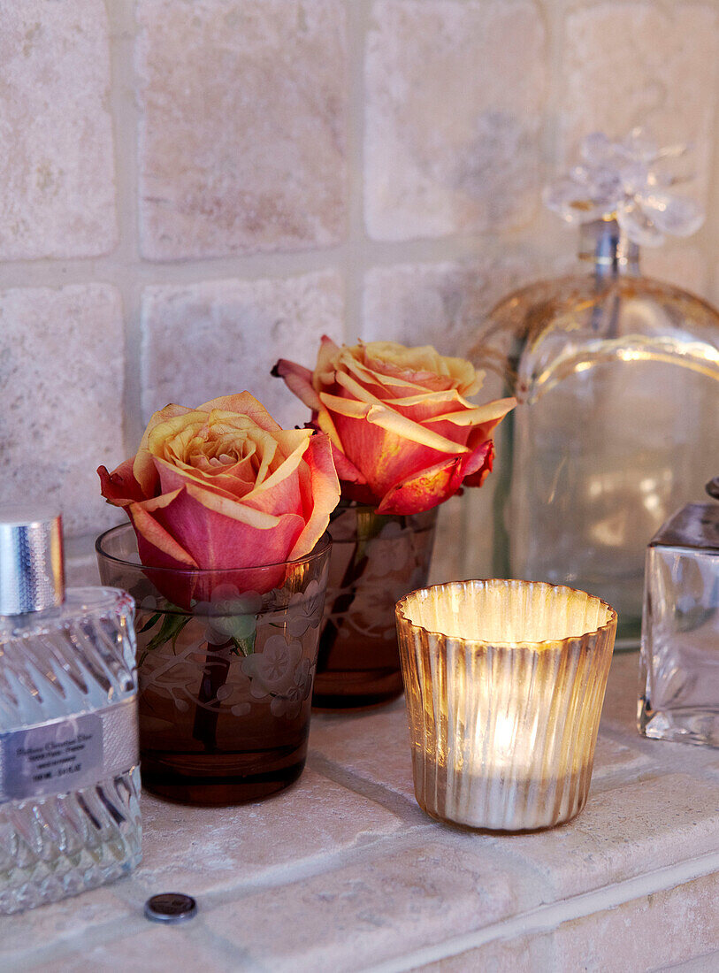 Geschnittene Rosen und brennende Kerze mit Parfümflaschen auf gefliestem Regal