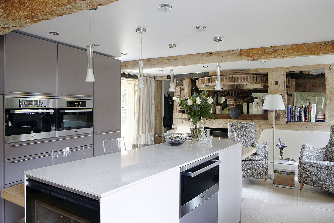 Open plan kitchen and living room with beamed ceiling in renovated Cotswolds mill house England UK