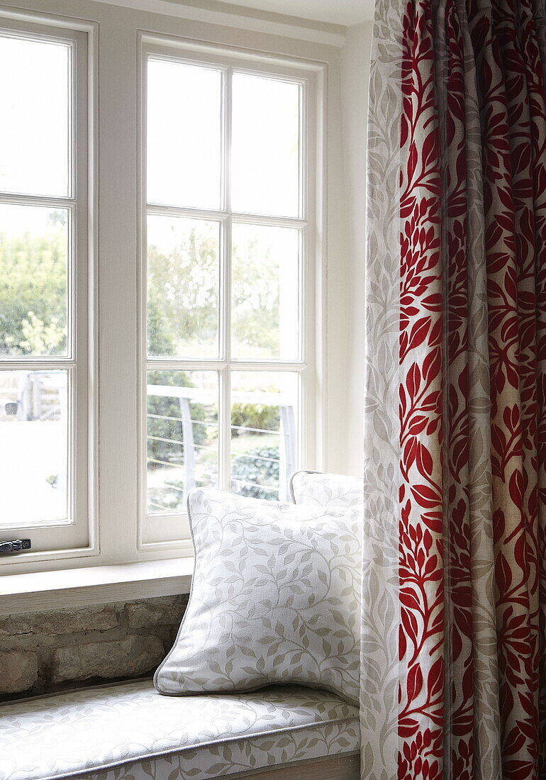 Red leaf motif curtains at window seat in renovated Cotswolds mill house England UK