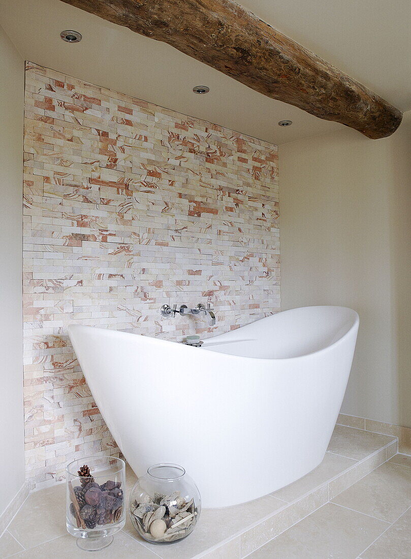 Freistehende Badewanne aus weißer Keramik und Deckenbalken in einem renovierten Mühlenhaus in den Cotswolds, England, UK